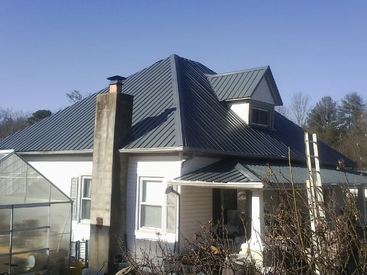 Dark blue standing seam metal roof on a white farmhouse with dormer — Slate & Tile Roof Repair by Roofing Brothers in Vestal