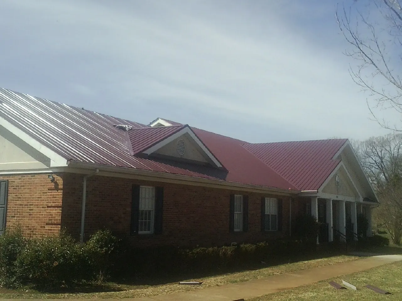 Red metal roof with gabled entries on a long brick building, from a Hail Damage Roof Repair job in Vestal