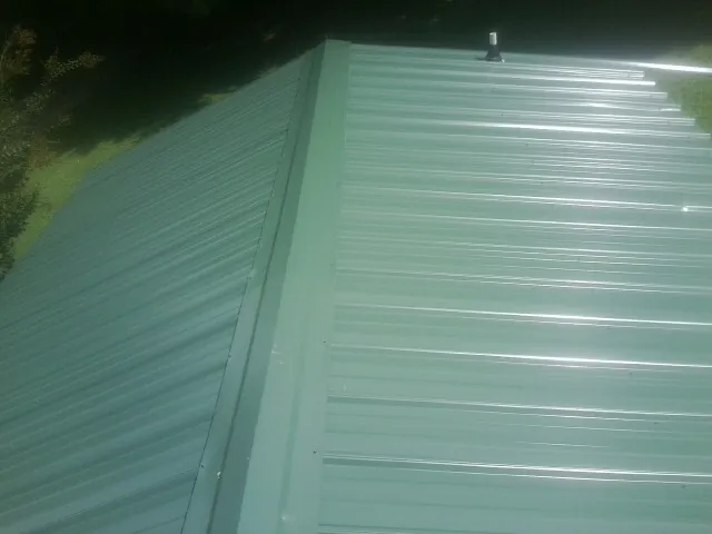 New green metal panels meeting at the ridge of a roof — Flat Roof Repair work by our crew in Vestal