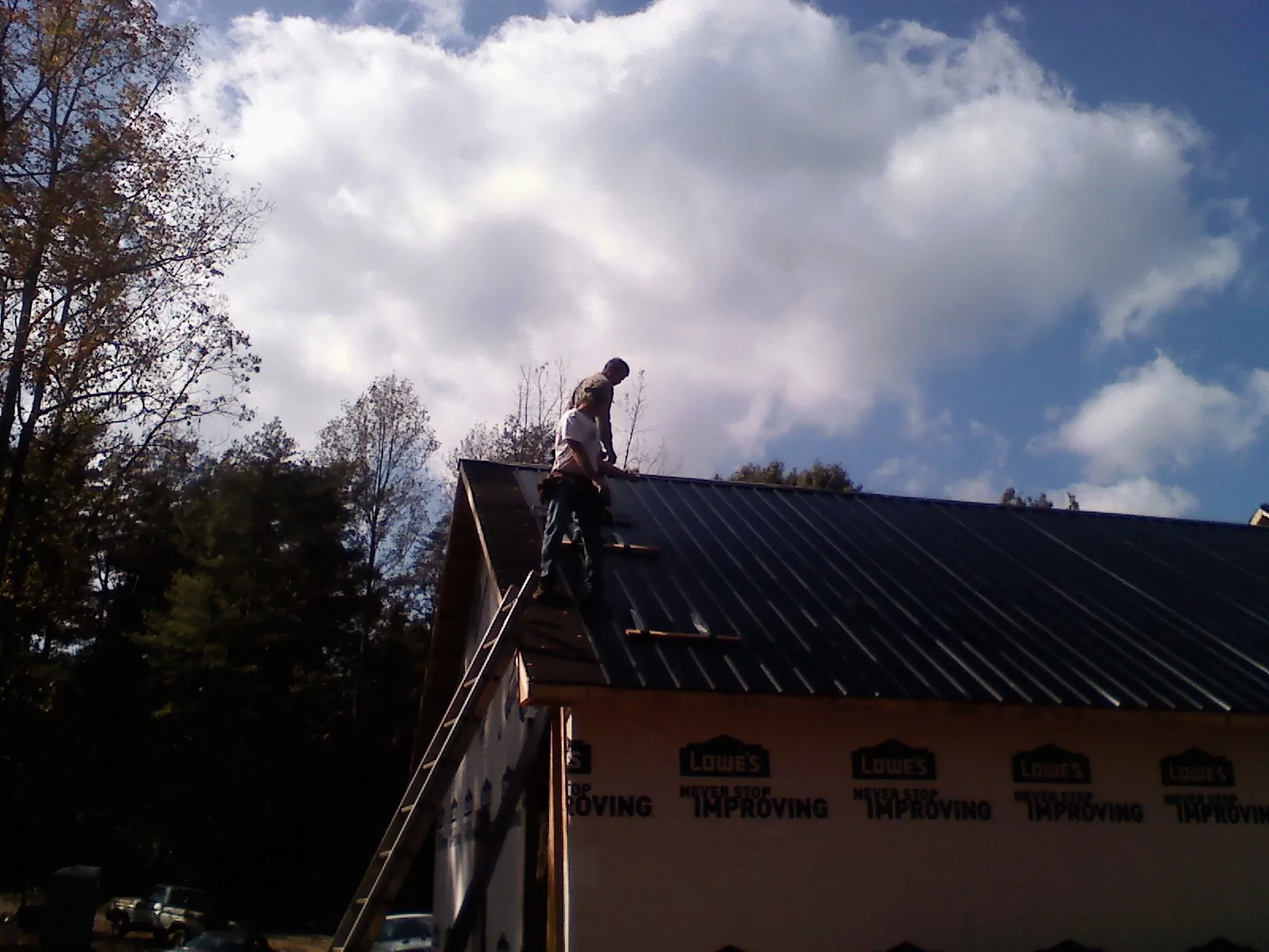 Roofer fastening dark metal panels high against a cloudy sky, from a Roof Inspection job in Vestal