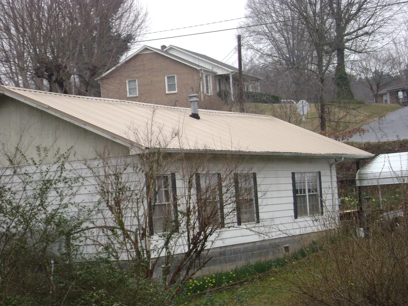 Tan metal roof on a white sided house set into a hillside — Commercial Roofing by Roofing Brothers in Vestal