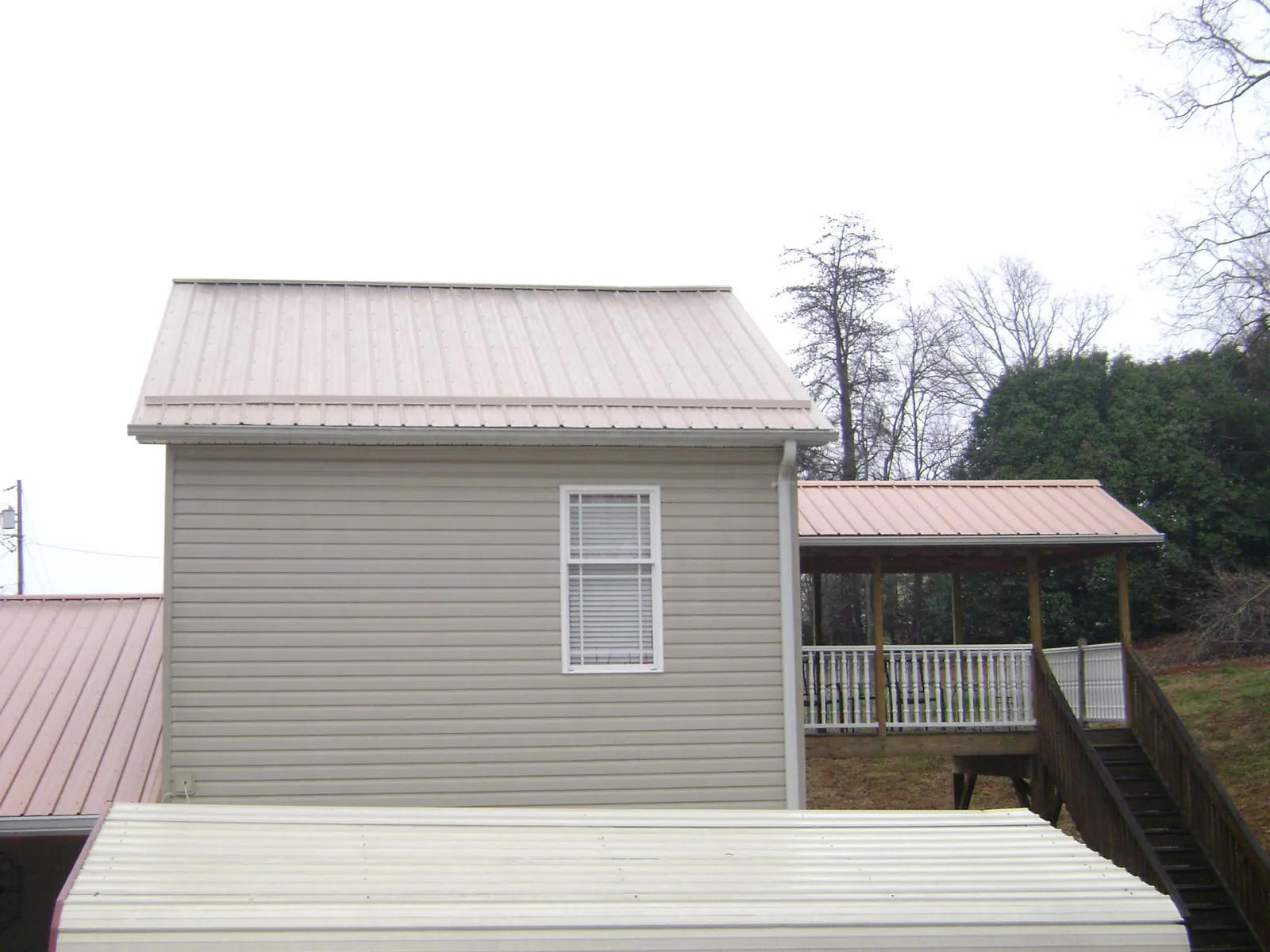 Tan metal roofs on a two story addition and attached porch, from a Roof Replacement job in Vestal